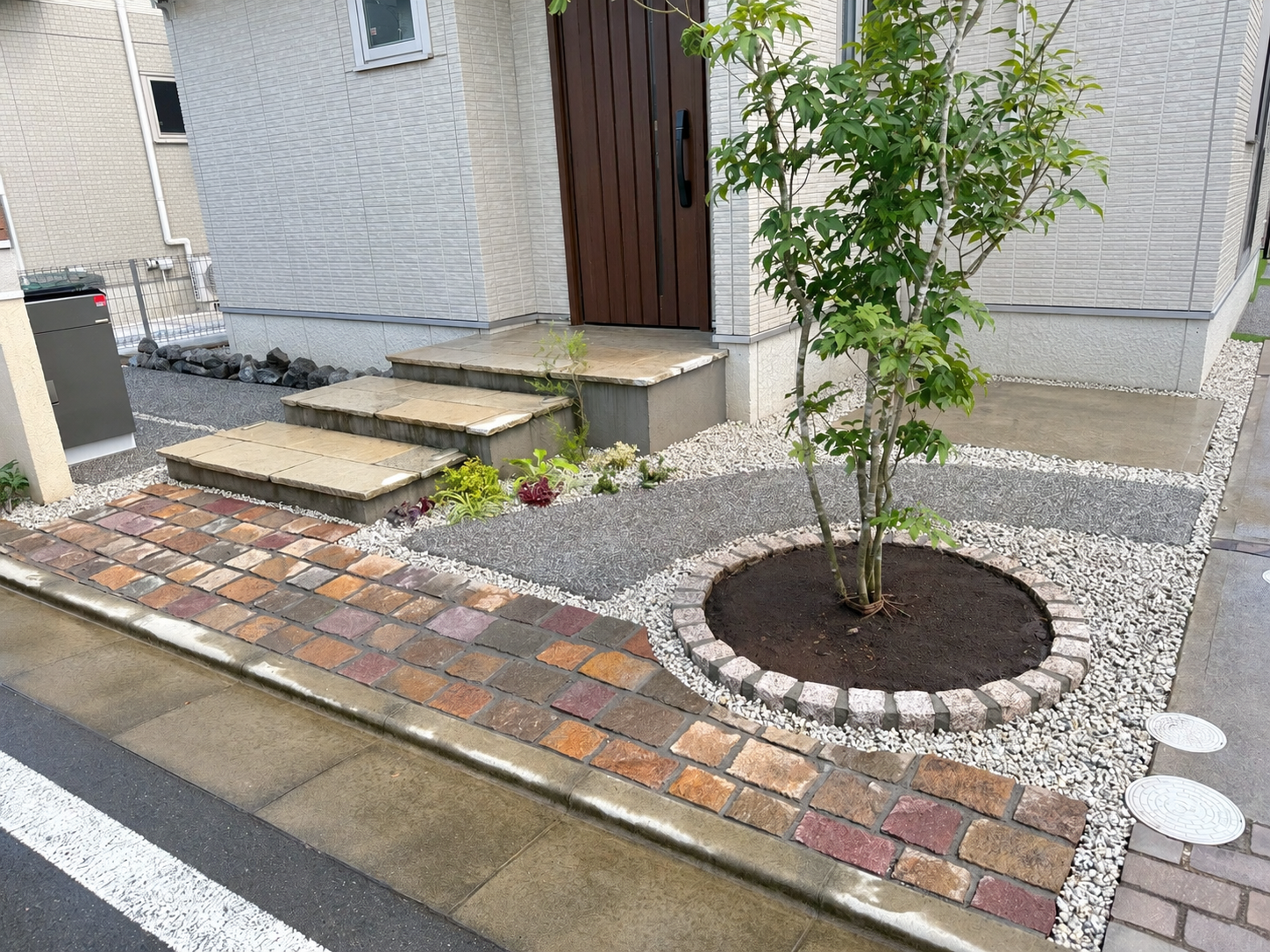 ピンコロ石で縁取ったサークル花壇とシンボルツリー、玄関まわりの植栽